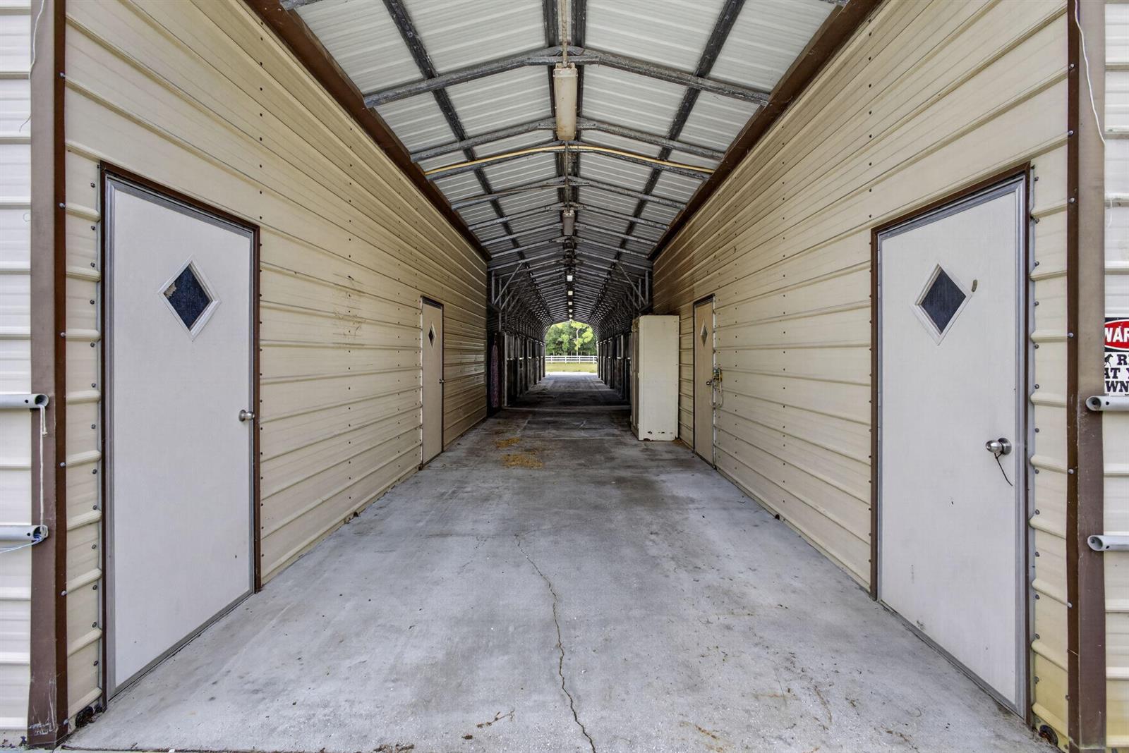 A covered outdoor walkway features metal siding, concrete flooring, and multiple doors leading to stalls — 2944 A Road, Loxahatchee FL 33470, LOXAHATCHEE, FL