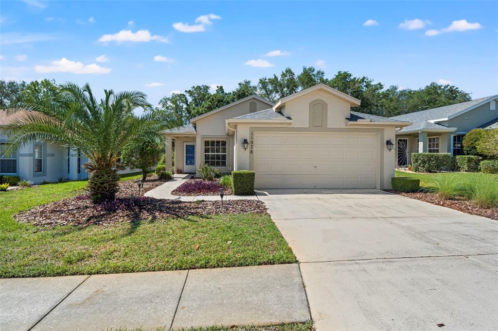 A single-story beige house with a two-car garage, a palm tree, and a concrete driveway — 11078 HEATHROW, SPRING HILL, FL