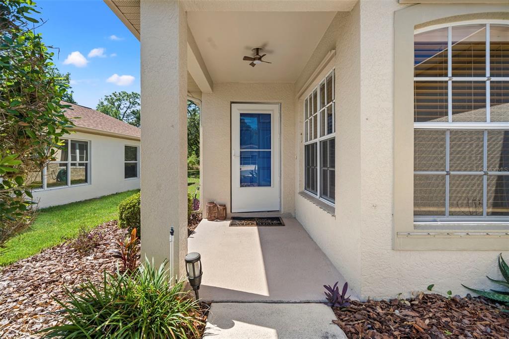 A covered front porch features a white door, a ceiling fan, and a welcome mat — 11078 HEATHROW, SPRING HILL, FL