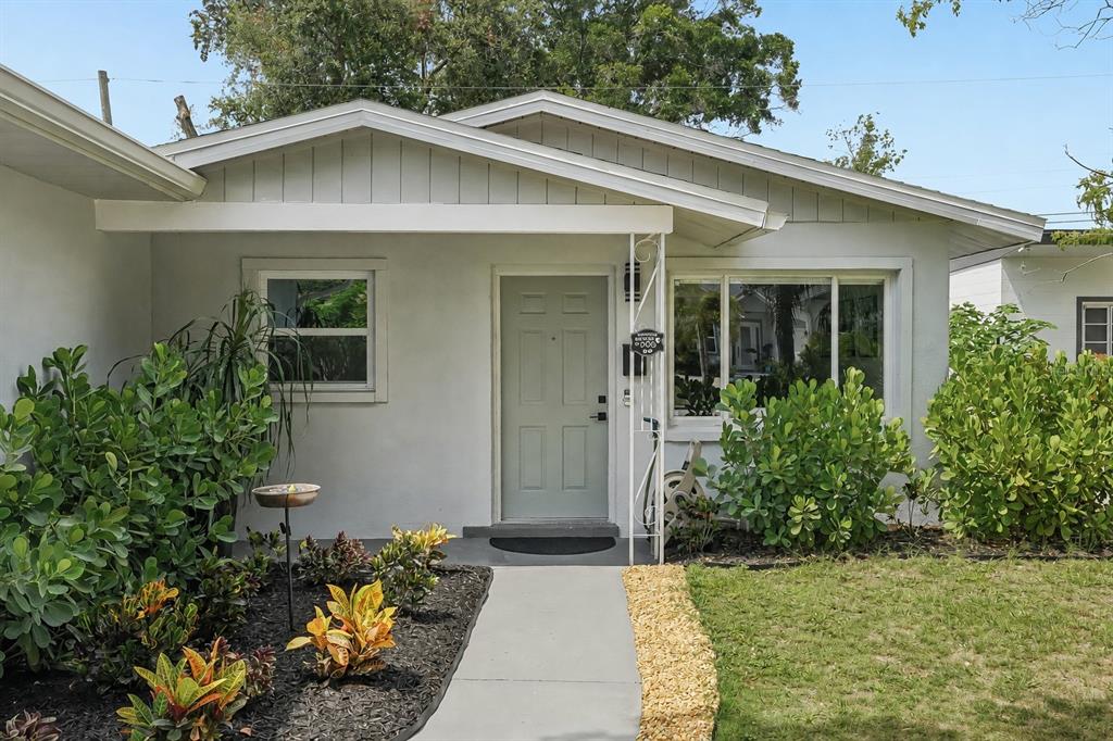 The exterior of a single-story house features a light gray door, white trim, and landscaping — 5043 14TH AVENUE N, ST PETERSBURG, FL