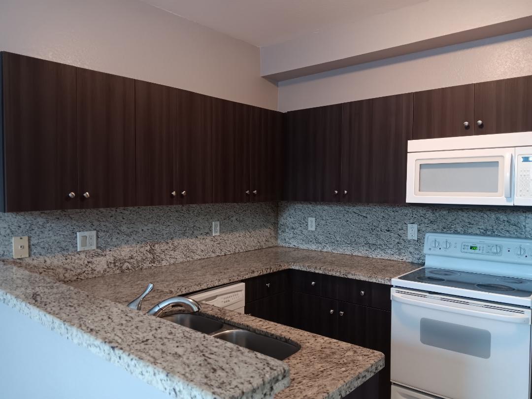 A kitchen features dark wood cabinets, granite countertops, and white appliances — 4321 SW 160th Avenue # 203, Miramar FL 33027, MIRAMAR, FL