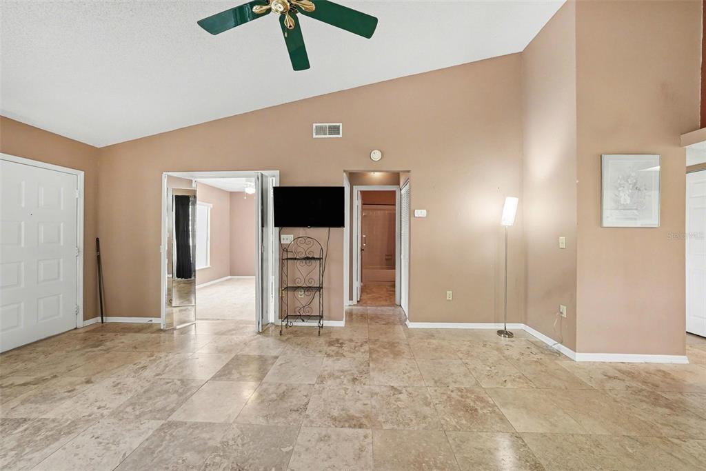 A living room with tan tile flooring, a vaulted ceiling, and a mounted television — 7816 HARDWICK DRIVE UNIT 1011, NEW PORT RICHEY, FL