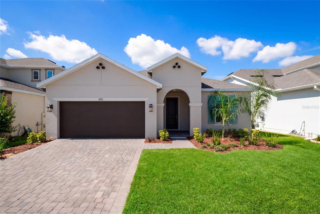 A single-story house with a beige stucco exterior, a brown garage door, and a paved driveway — 851 VINEYARD RIDGE ROAD NW, MINNEOLA, FL