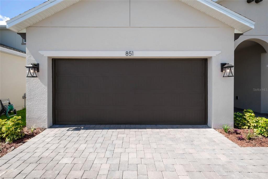 A beige house exterior features a dark brown garage door and a paved driveway — 851 VINEYARD RIDGE ROAD NW, MINNEOLA, FL