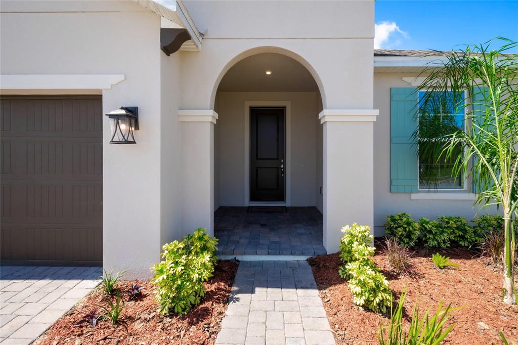 A front exterior view showing a paved walkway, arched entryway, and a brown garage door — 851 VINEYARD RIDGE ROAD NW, MINNEOLA, FL