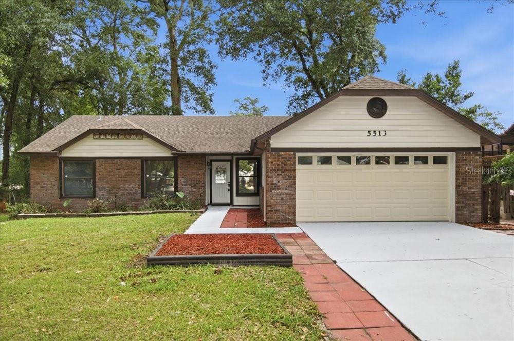A single-story brick house with a front-facing garage, a paved walkway, and a grassy lawn — 5513 CAURUS COURT, ORLANDO, FL
