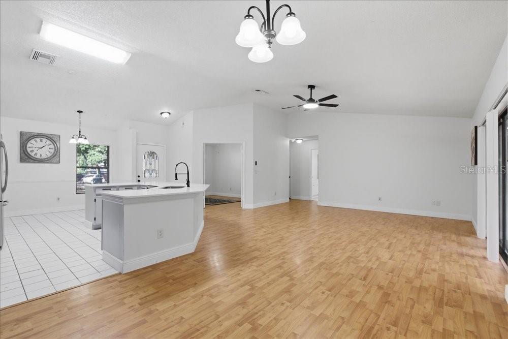 An open-concept kitchen and living area features light wood flooring, white cabinetry, and vaulted ceilings — 5513 CAURUS COURT, ORLANDO, FL