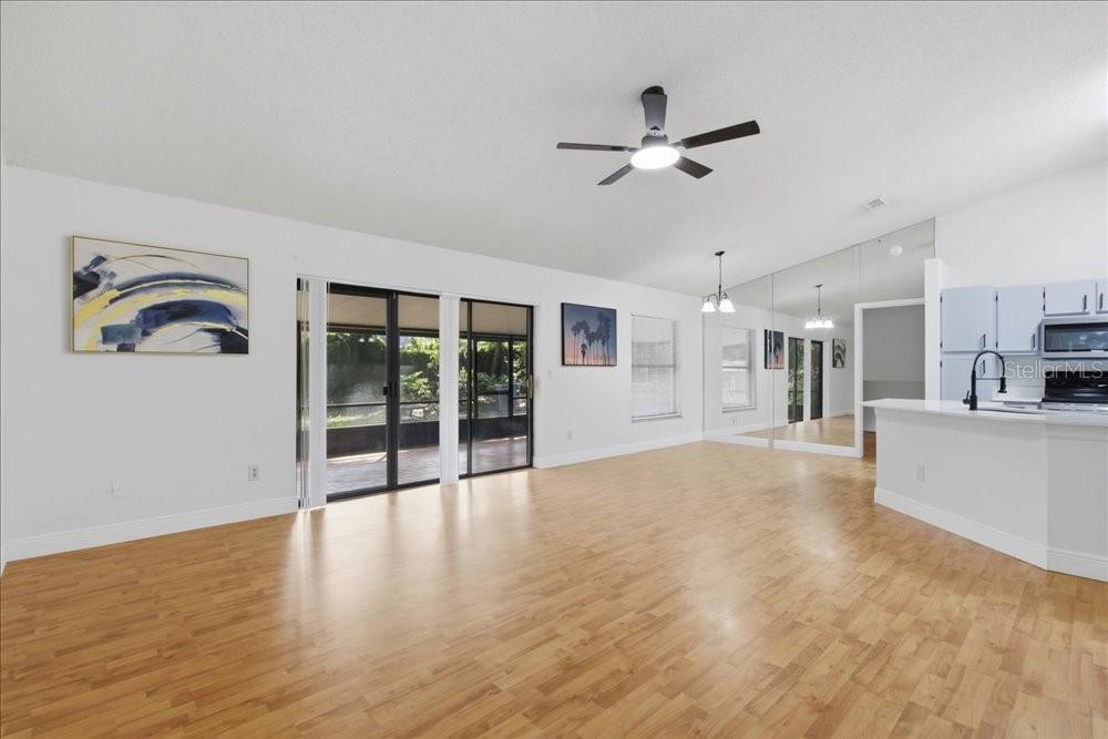 A living room with light wood flooring, a ceiling fan, and a mirrored wall — 5513 CAURUS COURT, ORLANDO, FL