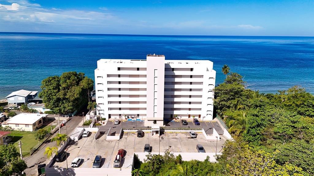 An aerial view shows a multi-story white apartment building situated along a blue ocean coastline — 429 C. PORTO VECCHIO UNIT 401, RINCON, PR
