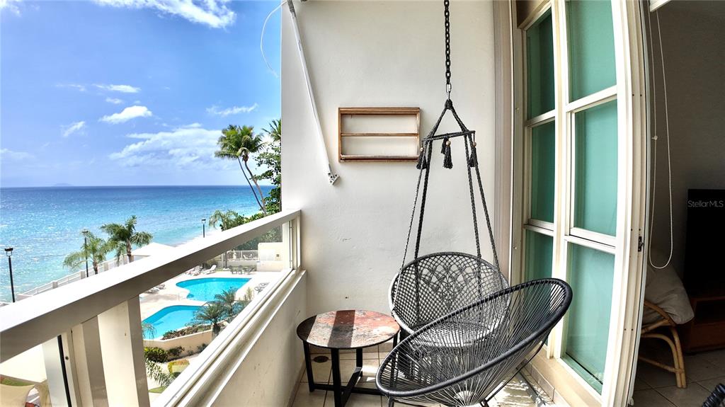 A balcony overlooks a swimming pool and the ocean, featuring a hanging chair and table — 429 C. PORTO VECCHIO UNIT 401, RINCON, PR