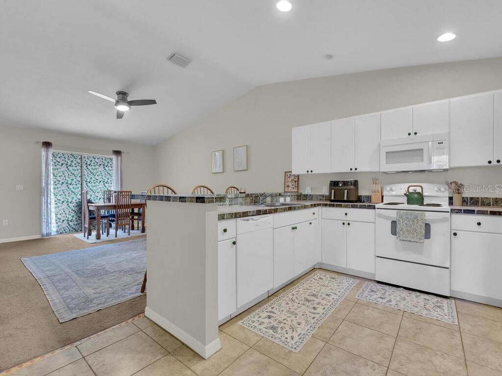 A kitchen with white cabinets and appliances overlooks a dining area with a sliding door — 1208/1210 SE 24TH AVENUE, CAPE CORAL, FL