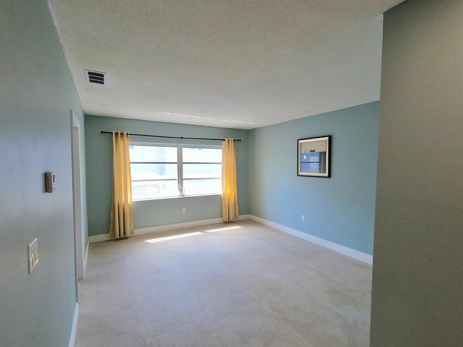 An empty room with light blue walls, tile flooring, and yellow curtains over a window — 382 E Royal Palm Road # 0080, Boca Raton FL 33432, BOCA RATON, FL