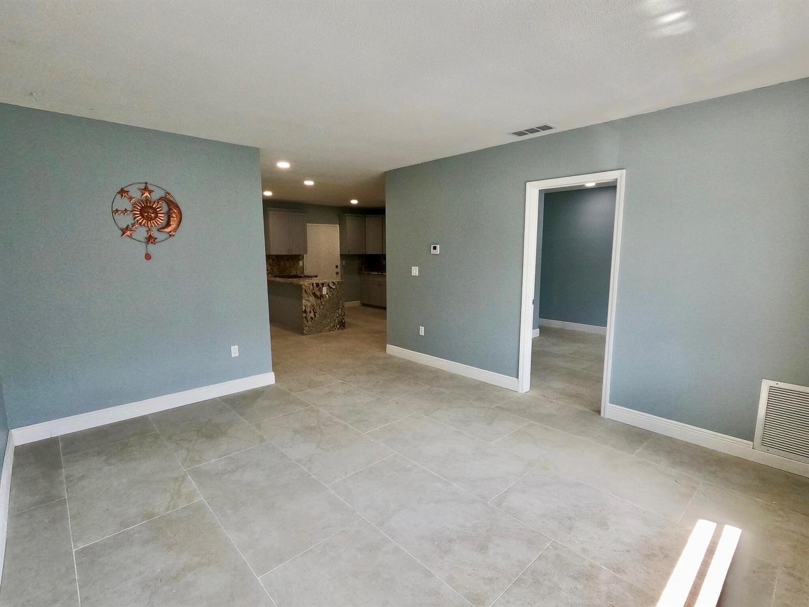 An open-concept living area features light blue walls, large gray floor tiles, and a kitchen — 382 E Royal Palm Road # 0080, Boca Raton FL 33432, BOCA RATON, FL