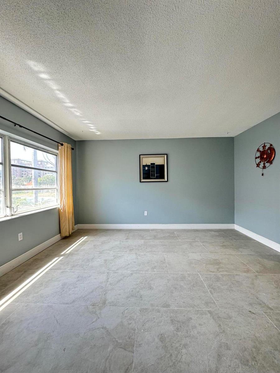 An empty room with light blue walls, large gray floor tiles, and a window — 382 E Royal Palm Road # 0080, Boca Raton FL 33432, BOCA RATON, FL