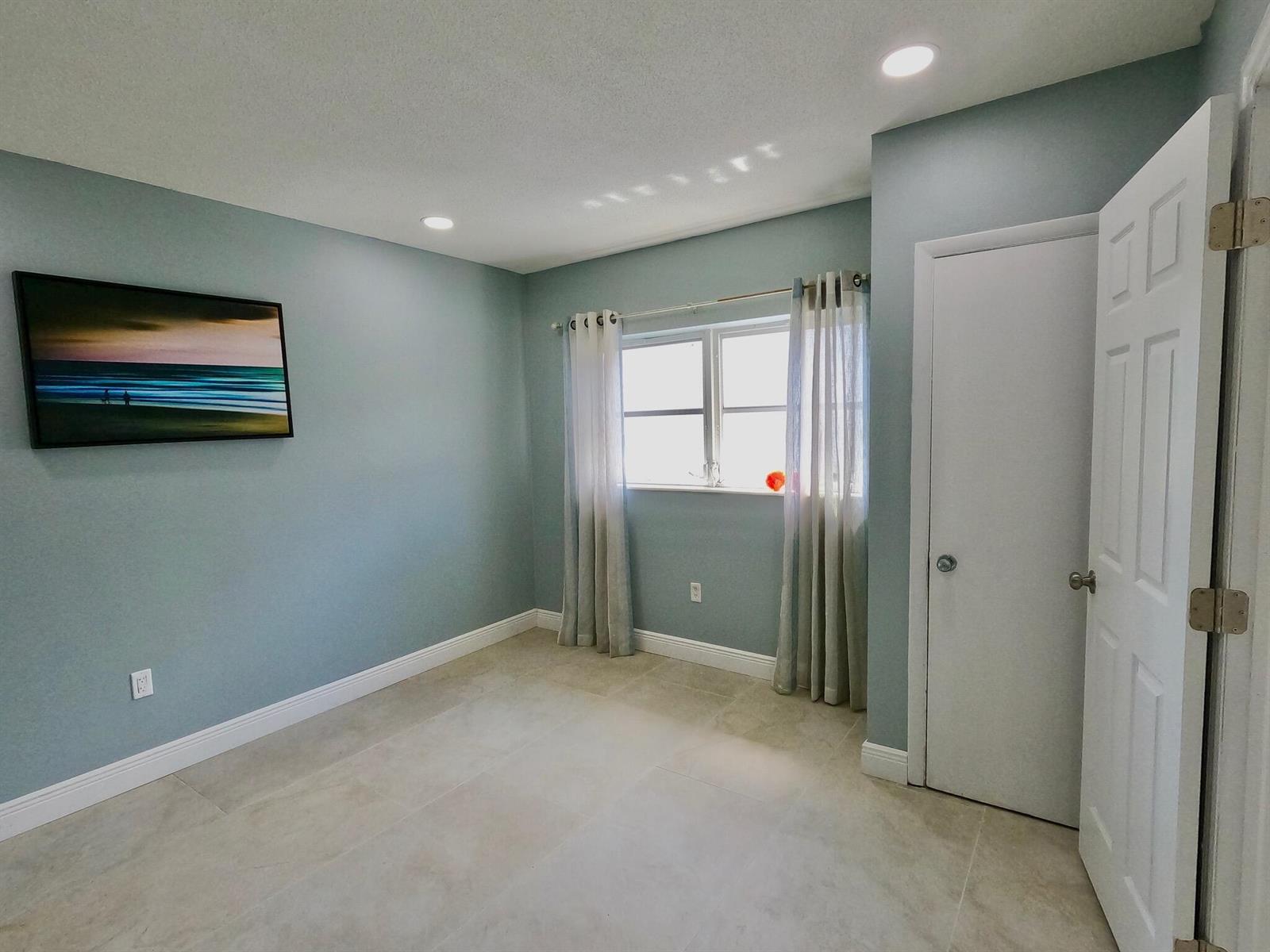 A bedroom with light blue walls, tile flooring, a window with curtains, and a closet — 382 E Royal Palm Road # 0080, Boca Raton FL 33432, BOCA RATON, FL