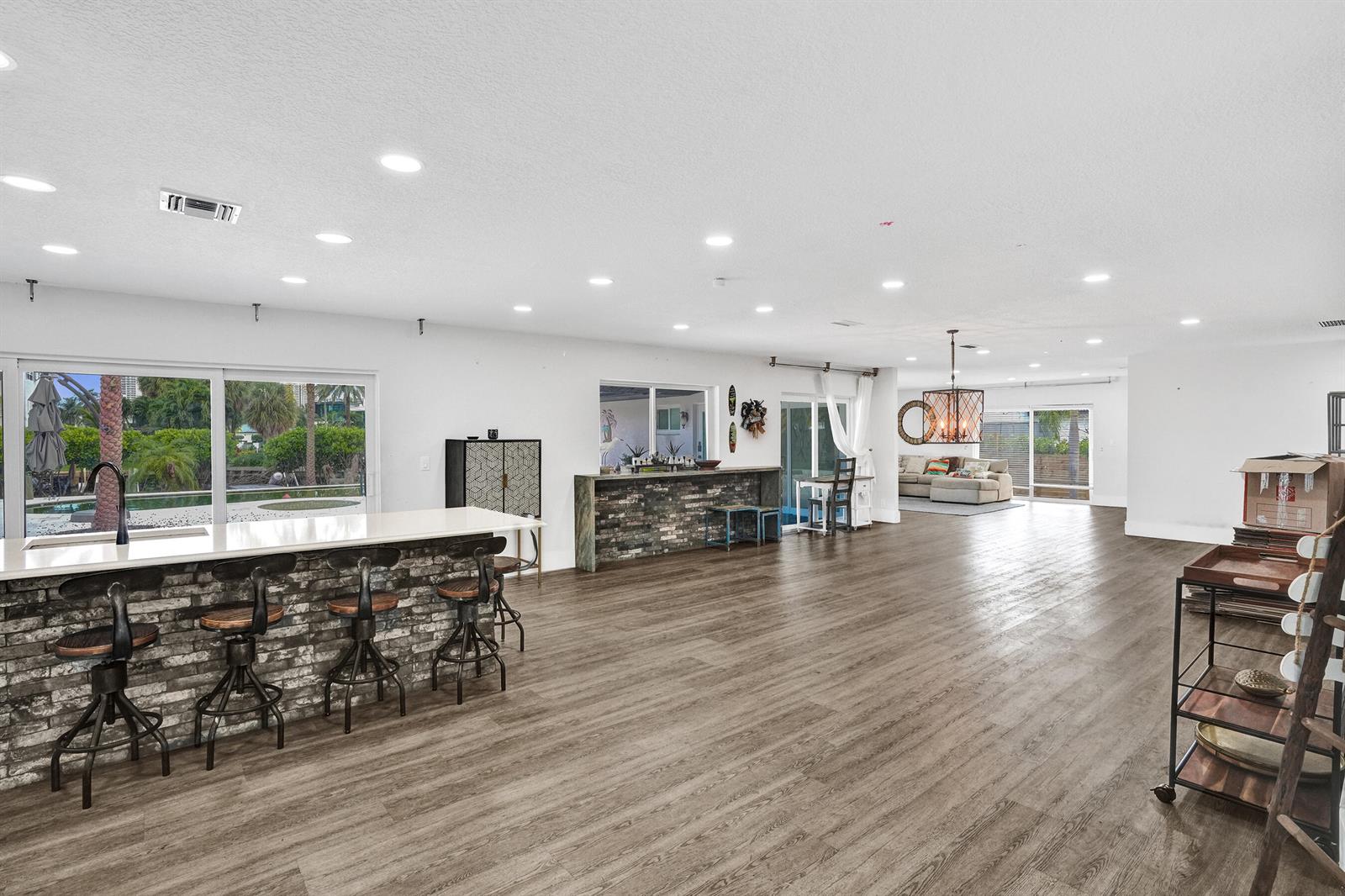 A spacious open-concept room features a brick-faced kitchen island, wood-look flooring, and sliding glass doors — 343 Layne Boulevard, Hallandale Beach FL 33009, HALLANDALE BEACH, FL