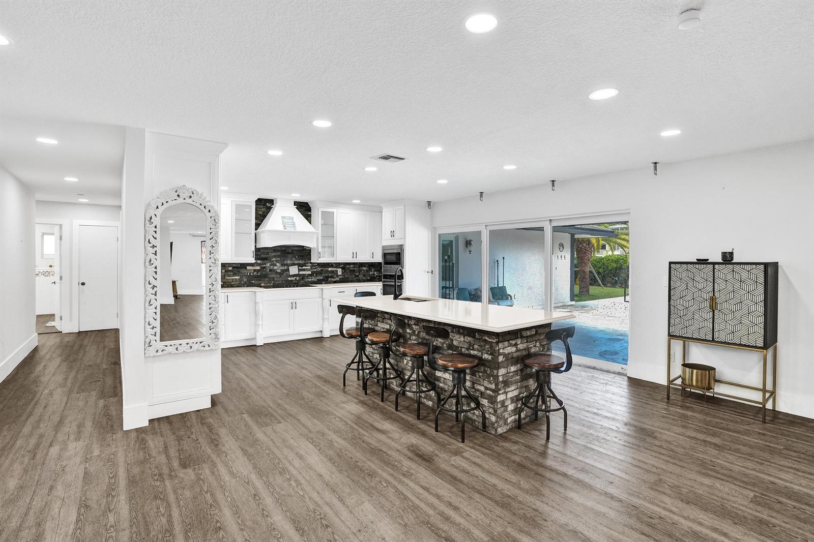 A kitchen features a brick-base island with bar stools, white cabinetry, and wood-look flooring — 343 Layne Boulevard, Hallandale Beach FL 33009, HALLANDALE BEACH, FL