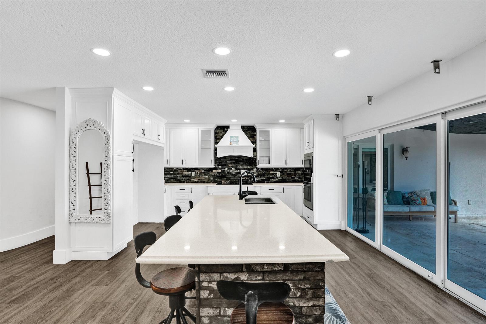 A modern kitchen features a large stone-base island, white cabinetry, and sliding glass patio doors — 343 Layne Boulevard, Hallandale Beach FL 33009, HALLANDALE BEACH, FL