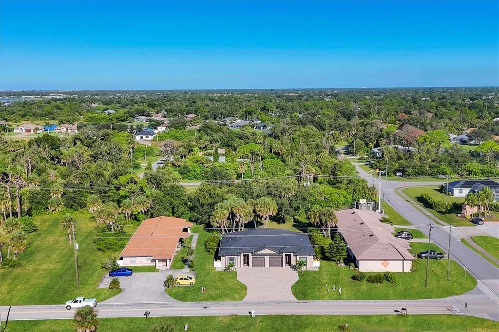 An aerial view shows three single-story houses situated along a road amidst dense green trees — 357 BOUNDARY BOULEVARD, ROTONDA WEST, FL