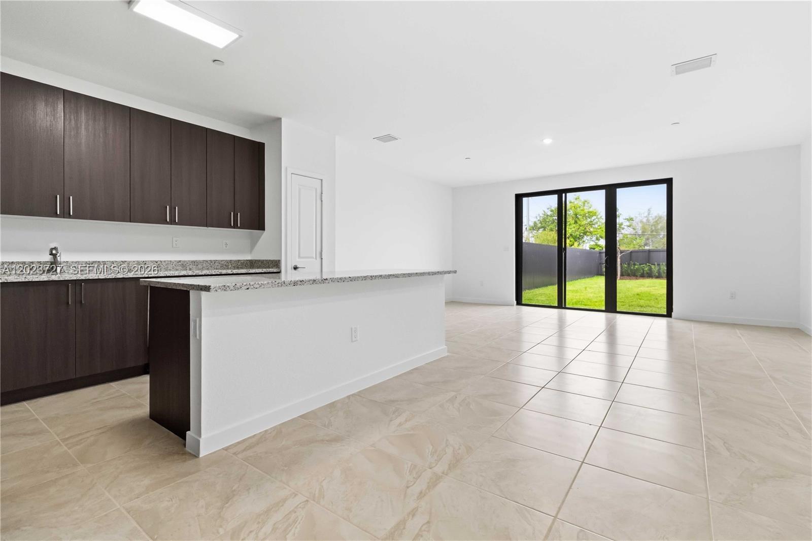 A kitchen with dark cabinets and a granite island opens to a tiled living area — 22348 SW 115 Ct # 22348, Miami FL 33170, MIAMI, FL