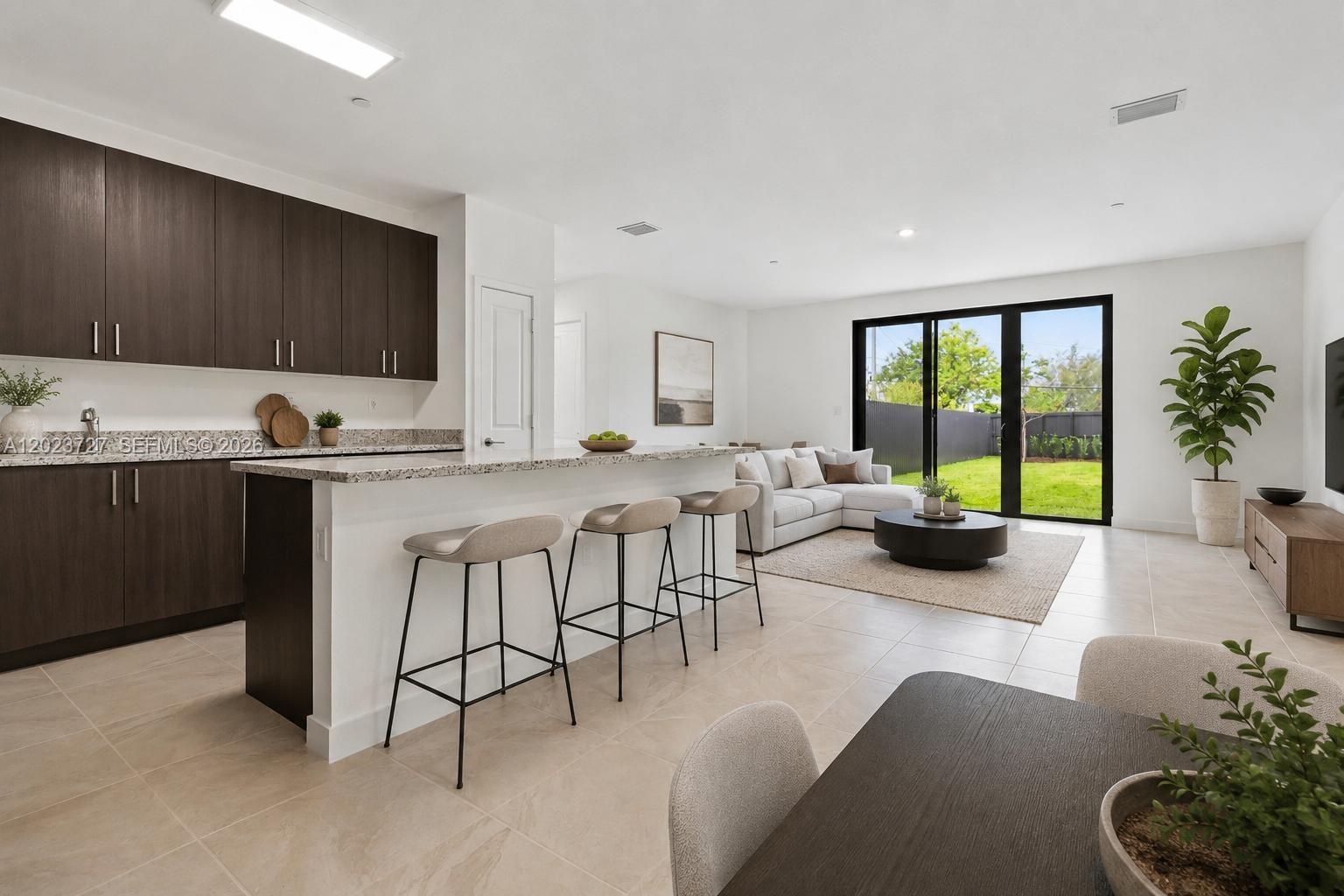 A modern open-concept kitchen and living area features dark wood cabinetry, a granite island, and patio access — 22348 SW 115 Ct # 22348, Miami FL 33170, MIAMI, FL