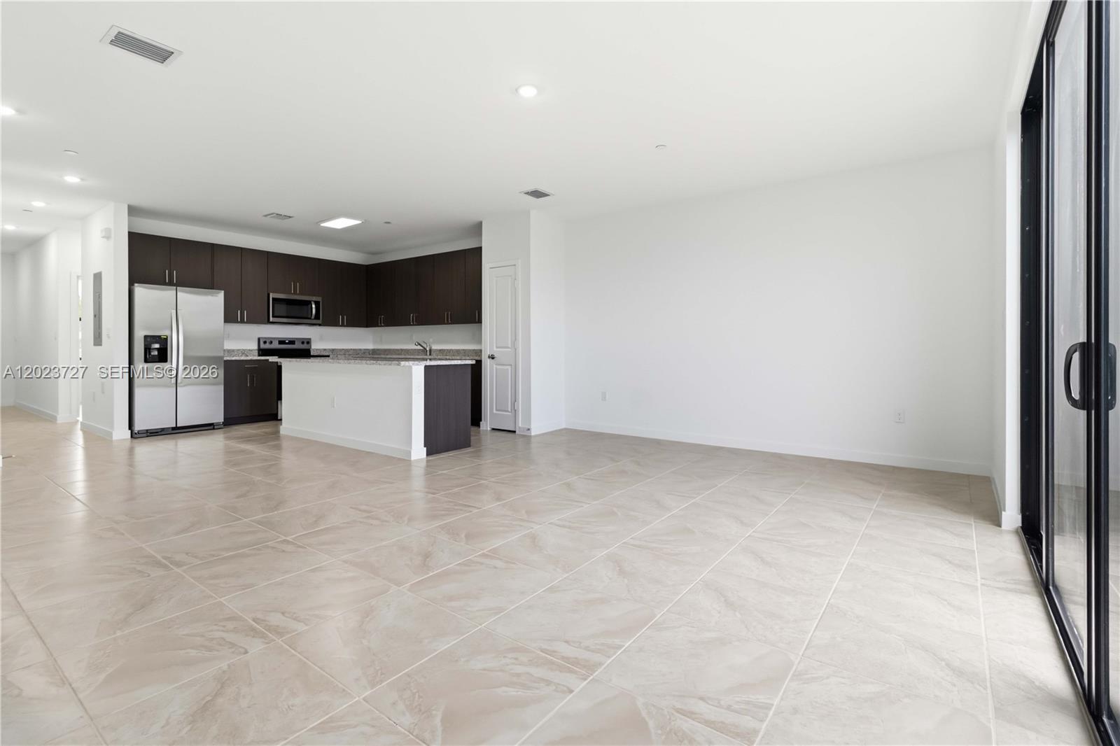 An open-concept kitchen with dark cabinets and a granite island overlooks a tiled living area — 22348 SW 115 Ct # 22348, Miami FL 33170, MIAMI, FL