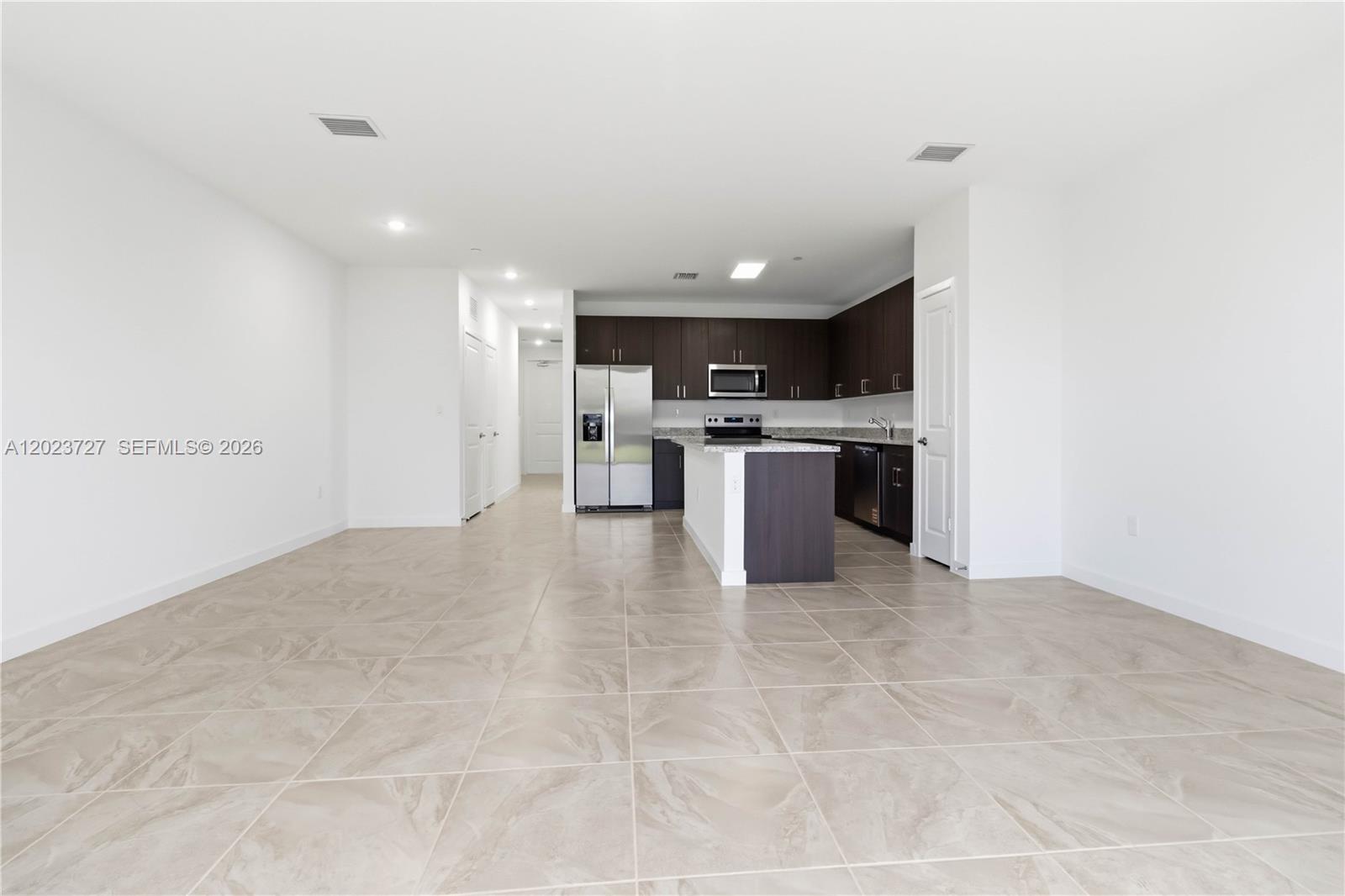 An open-concept kitchen features dark wood cabinets, stainless steel appliances, and light-colored tile flooring — 22348 SW 115 Ct # 22348, Miami FL 33170, MIAMI, FL