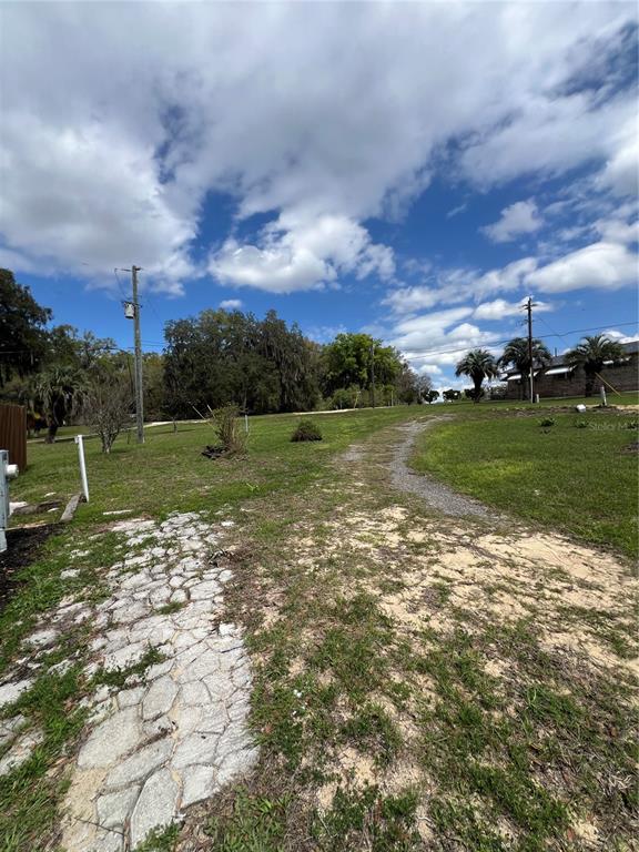 A grassy lot features a stone path leading toward trees under a cloudy blue sky — 6287 MAGNOLIA STREET, KEYSTONE HEIGHTS, FL