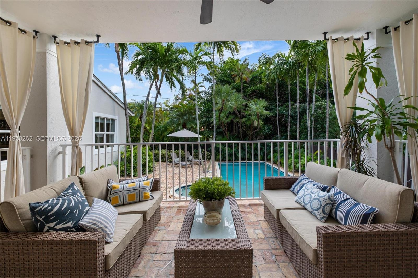 A covered patio features two wicker sofas, a coffee table, and a view of a pool — 164 W Mashta Dr, Key Biscayne FL 33149, KEY BISCAYNE, FL