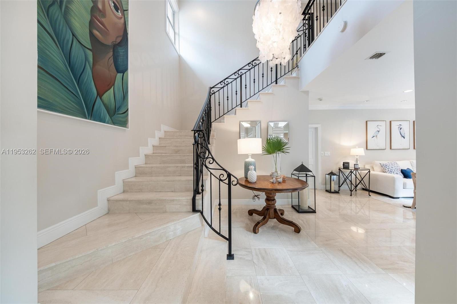 A grand foyer features a curved staircase with iron railings and light-colored stone flooring — 164 W Mashta Dr, Key Biscayne FL 33149, KEY BISCAYNE, FL