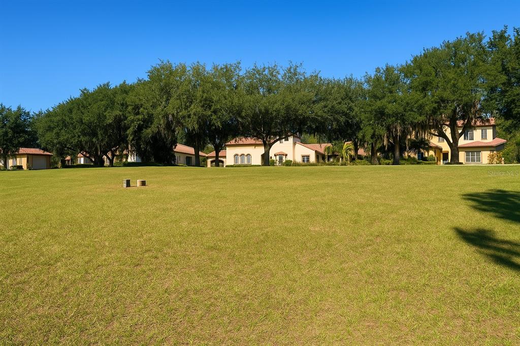 A large, grassy lawn leads to a multi-story house surrounded by mature oak trees — 9509 SAN FERNANDO COURT, HOWEY IN THE HILLS, FL
