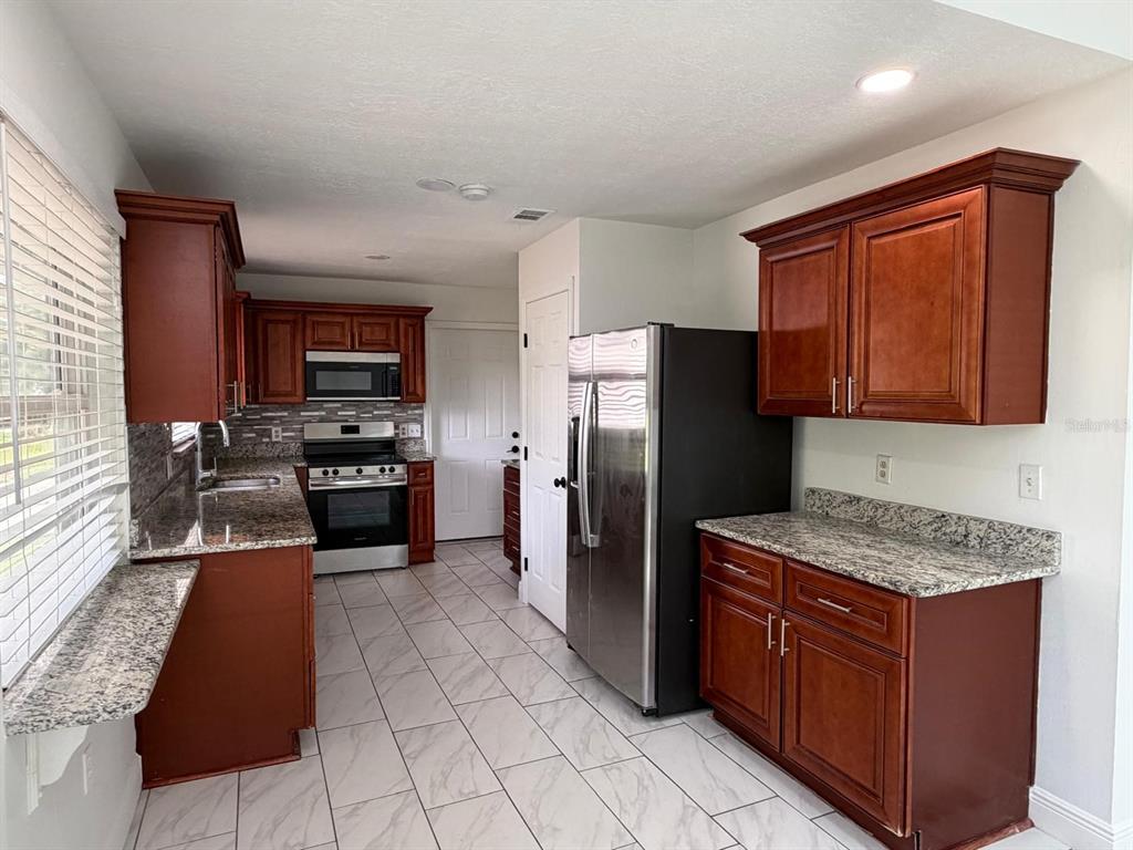 A kitchen features dark wood cabinets, granite countertops, stainless steel appliances, and light tile flooring — 2356 ROYALE OAKS BOULEVARD, KISSIMMEE, FL