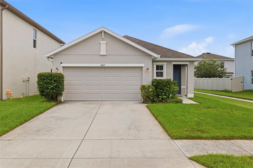 A single-story house with a beige stucco exterior, a two-car garage, and a front lawn — 16163 SILENT SANDS LANE, ODESSA, FL
