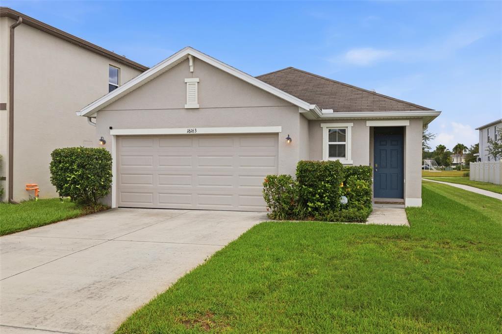 A single-story house with a beige stucco exterior, a two-car garage, and a blue door — 16163 SILENT SANDS LANE, ODESSA, FL