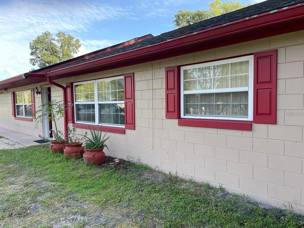 The exterior of a beige concrete block house features red shutters, trim, and a roofline — 1212 SHAWNEE DRIVE, KISSIMMEE, FL