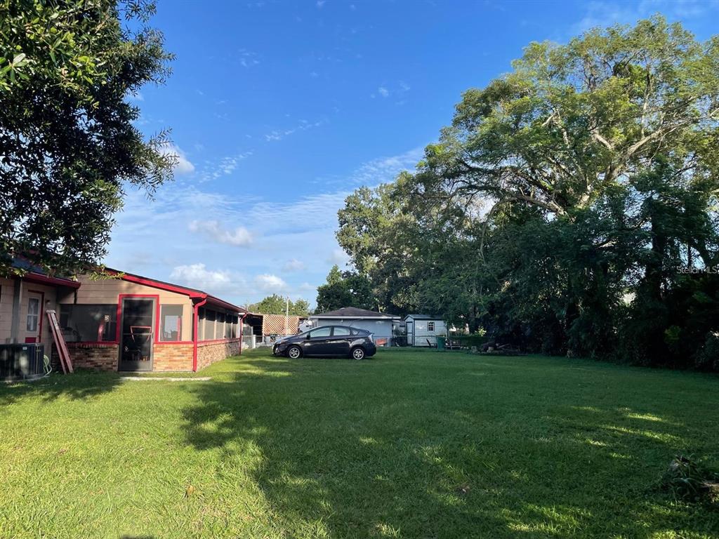 A large, grassy backyard features a dark car parked near a house with a screened porch — 1212 SHAWNEE DRIVE, KISSIMMEE, FL