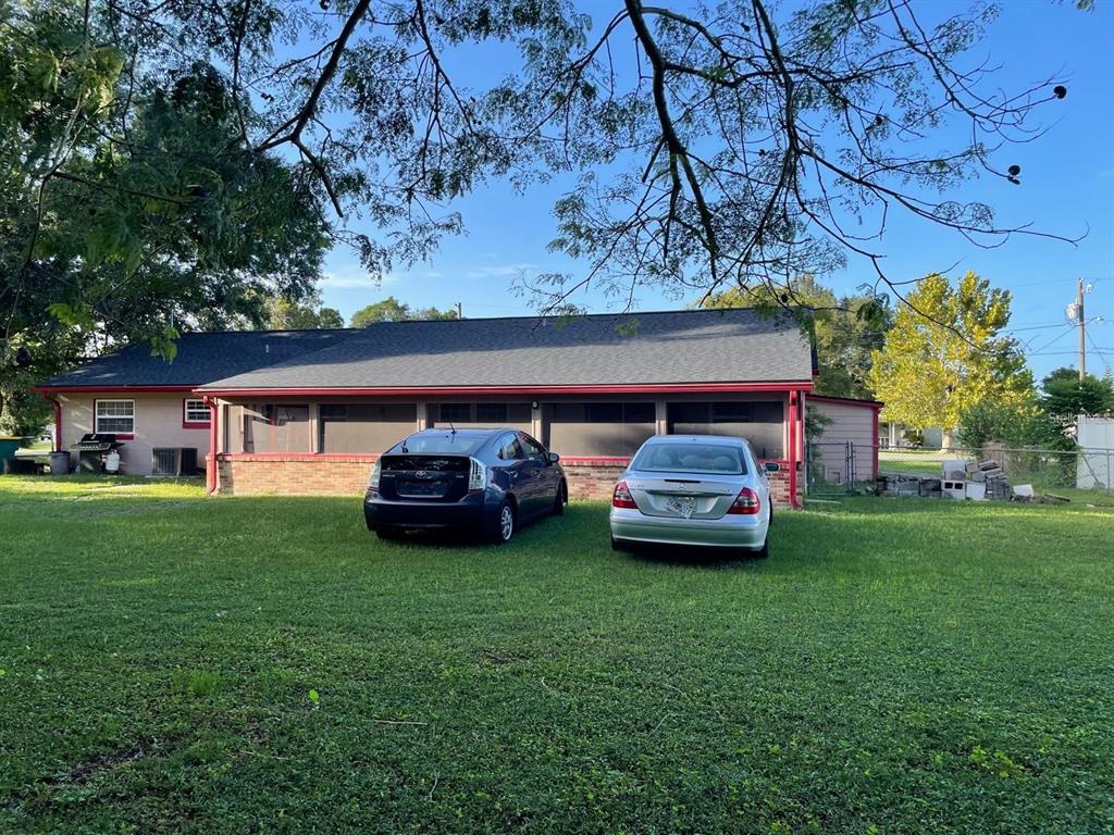 A single-story house with a screened porch and two cars parked on the lawn — 1212 SHAWNEE DRIVE, KISSIMMEE, FL