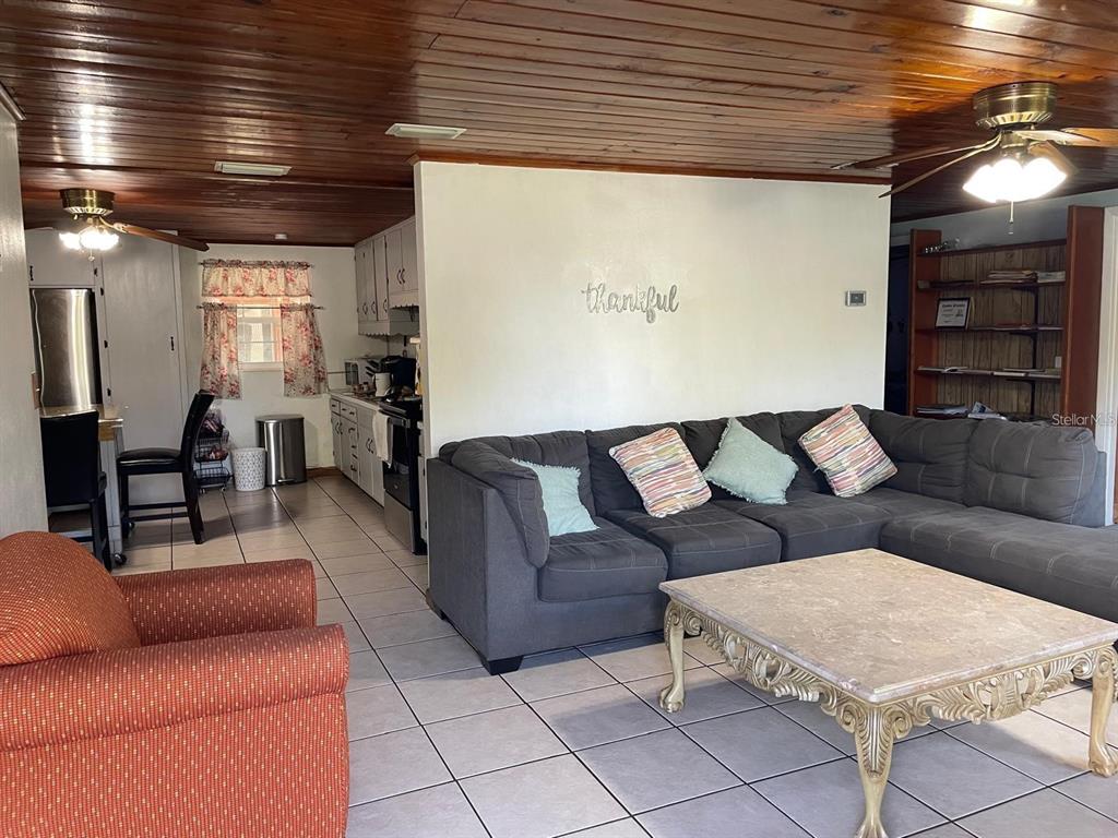 A living room with a gray sectional sofa, tile floors, and a wood-paneled ceiling — 1212 SHAWNEE DRIVE, KISSIMMEE, FL