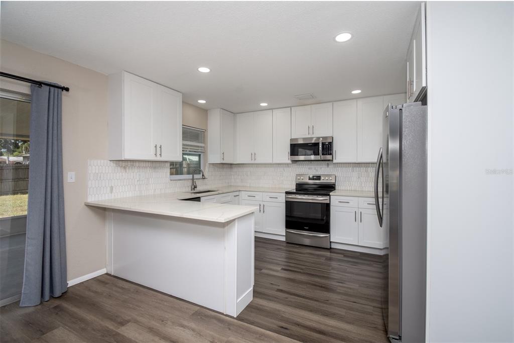 A kitchen with white cabinets, stainless steel appliances, quartz countertops, and wood-look flooring — 1531 VALENCIA STREET, CLEARWATER, FL