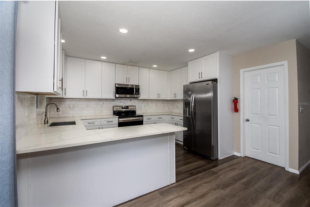 A kitchen features white cabinets, stainless steel appliances, a peninsula, and light-colored countertops — 1531 VALENCIA STREET, CLEARWATER, FL