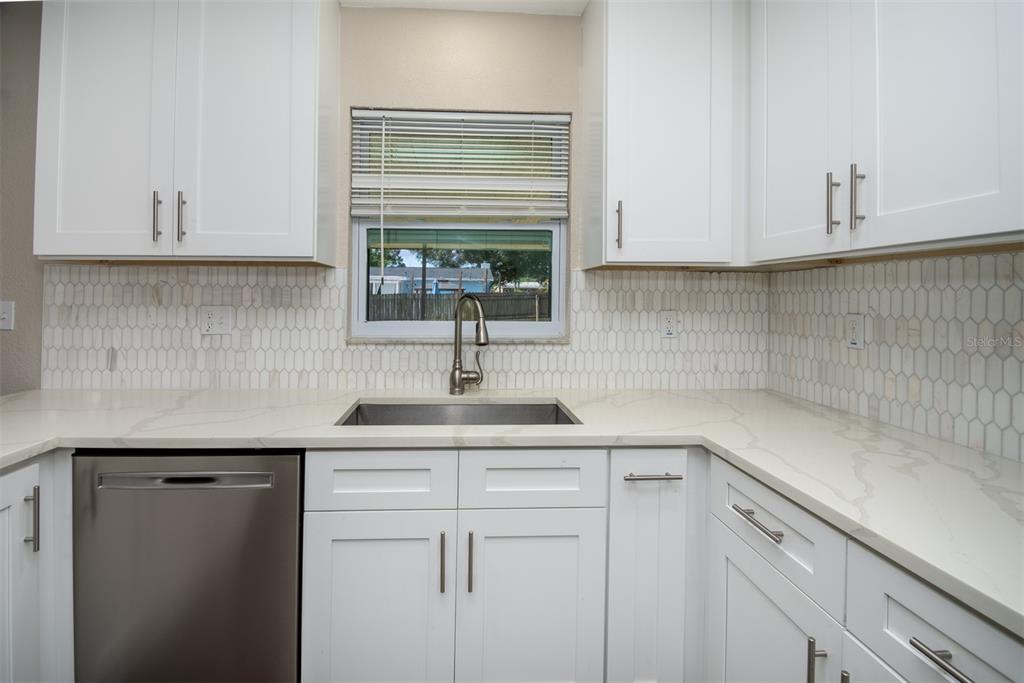 A kitchen features white cabinets, a stainless steel dishwasher, a sink, and a tiled backsplash — 1531 VALENCIA STREET, CLEARWATER, FL