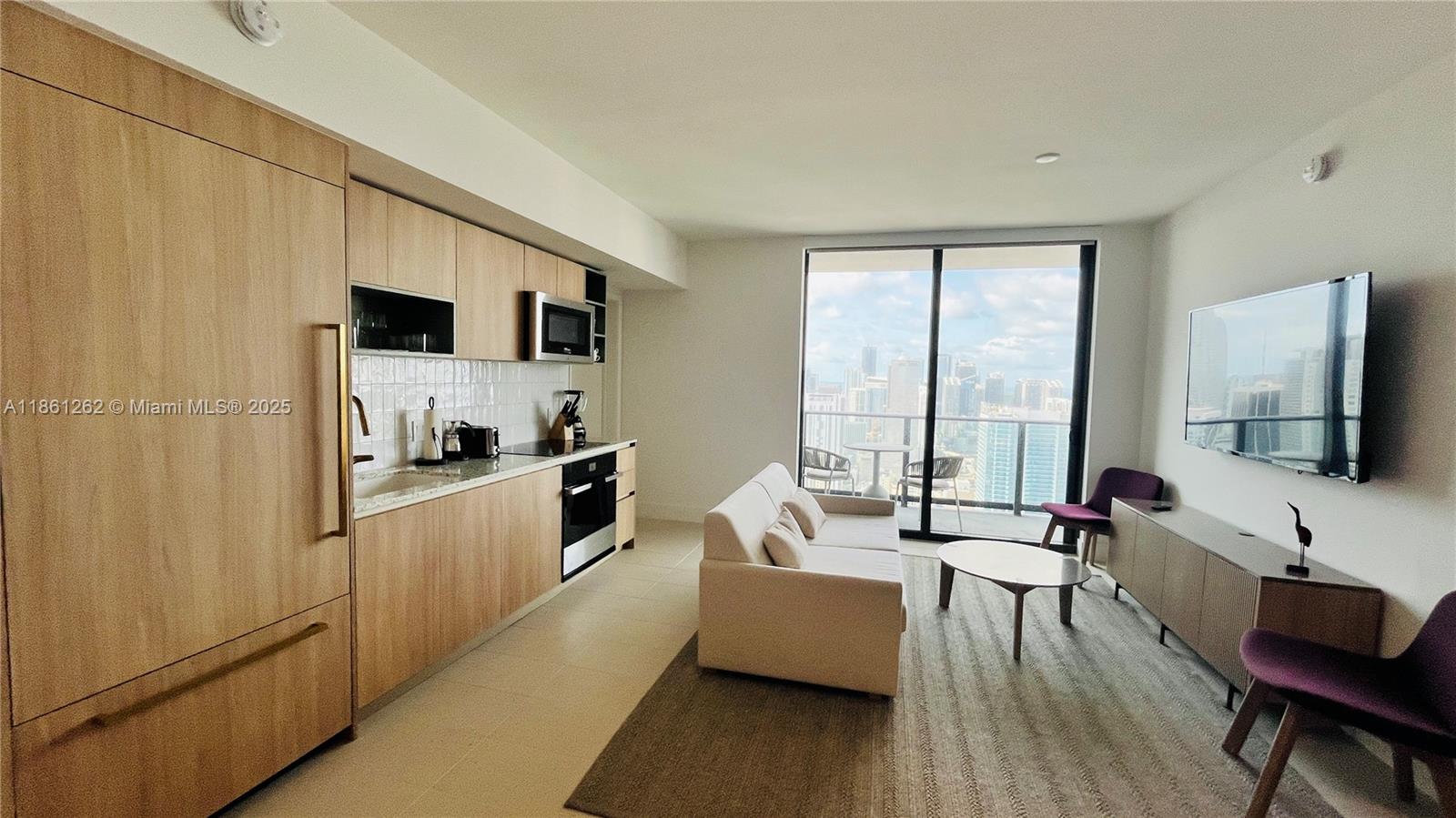 A modern apartment features a kitchen with light wood cabinetry, a living area, and balcony — 159 NE 6th St # 4605, Miami FL 33132, MIAMI, FL