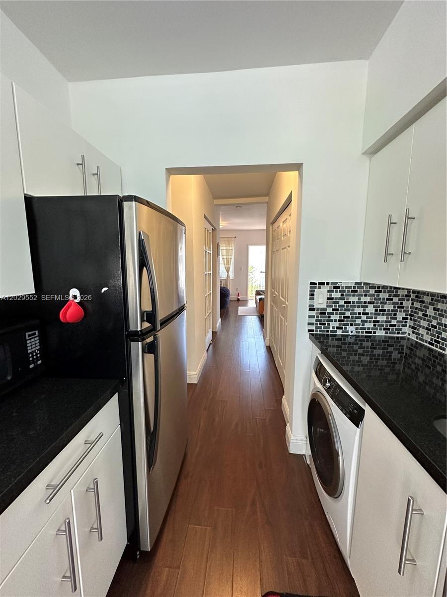 A galley-style kitchen features white cabinets, black countertops, a stainless refrigerator, and a washer — 911 Meridian Ave # 206, Miami Beach FL 33139, MIAMI BEACH, FL