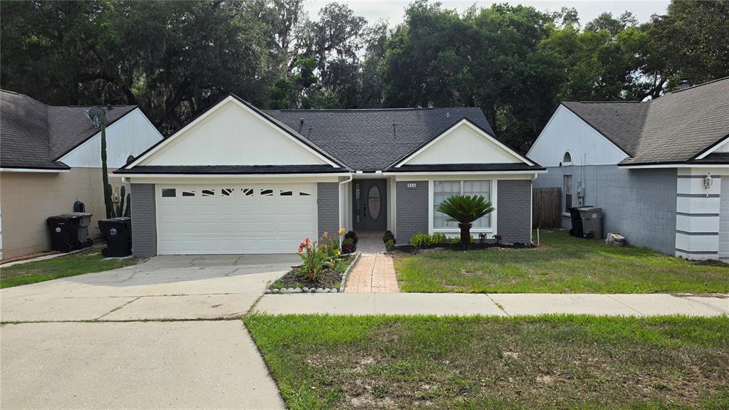 A single-story house with a white garage, gray brick facade, and a paved walkway — 204 N CERVIDAE DRIVE, APOPKA, FL
