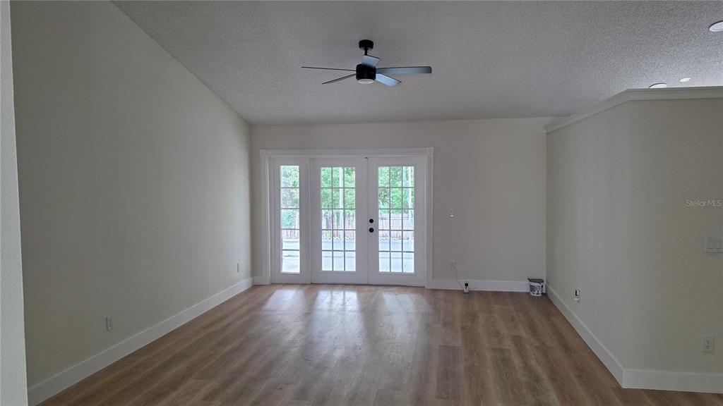 An empty room features light wood-look flooring, white walls, a ceiling fan, and French doors — 204 N CERVIDAE DRIVE, APOPKA, FL