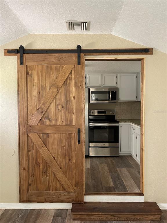 A wooden barn door opens to a kitchen with stainless steel appliances and white cabinets — 5830 ALLIGATOR LAKE SHORE W, ST CLOUD, FL