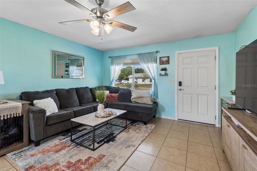 A living room features a grey sectional sofa, a coffee table, and light blue walls — 6882 62ND AVENUE N, PINELLAS PARK, FL