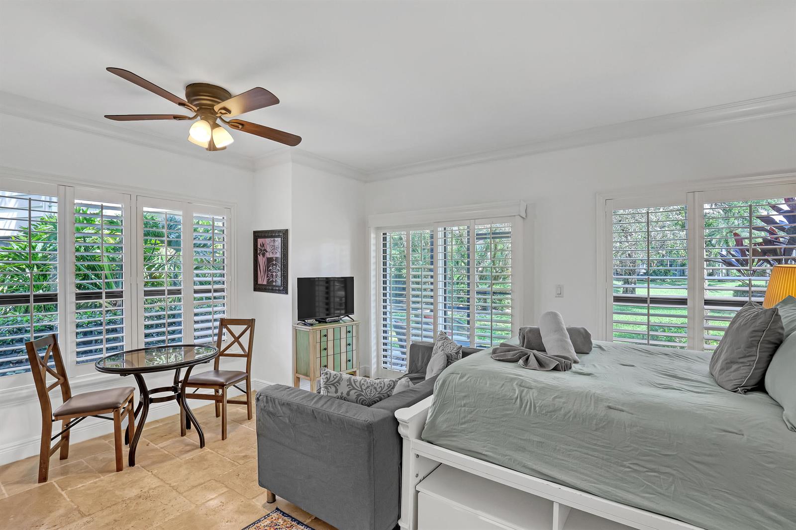 A bedroom features a bed, a small dining table, a sofa, and plantation shutters — 11863 Wimbledon Circle # 408, Wellington FL 33414, WELLINGTON, FL
