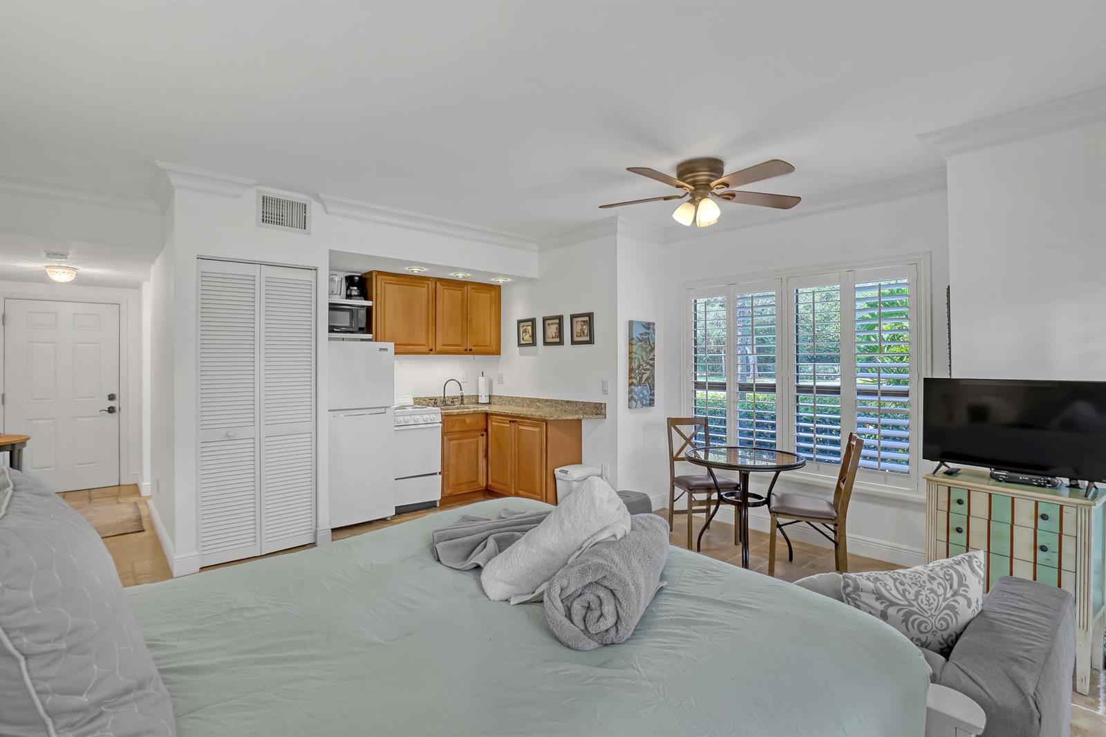A studio apartment features a bed, a small kitchenette with wooden cabinets, and a dining set — 11863 Wimbledon Circle # 408, Wellington FL 33414, WELLINGTON, FL