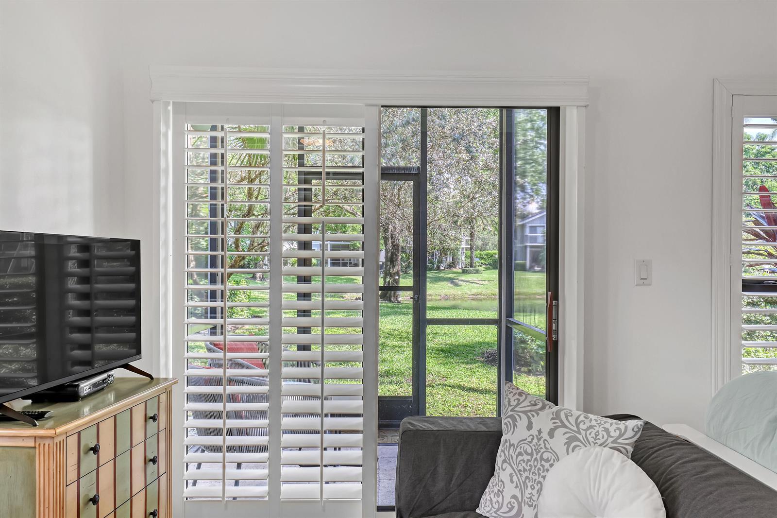 A living room features a television, a dresser, a sofa, and sliding glass doors with shutters — 11863 Wimbledon Circle # 408, Wellington FL 33414, WELLINGTON, FL